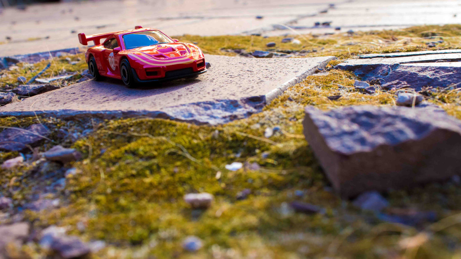 Small red car pictured on a concrete tile surrounded by moss.